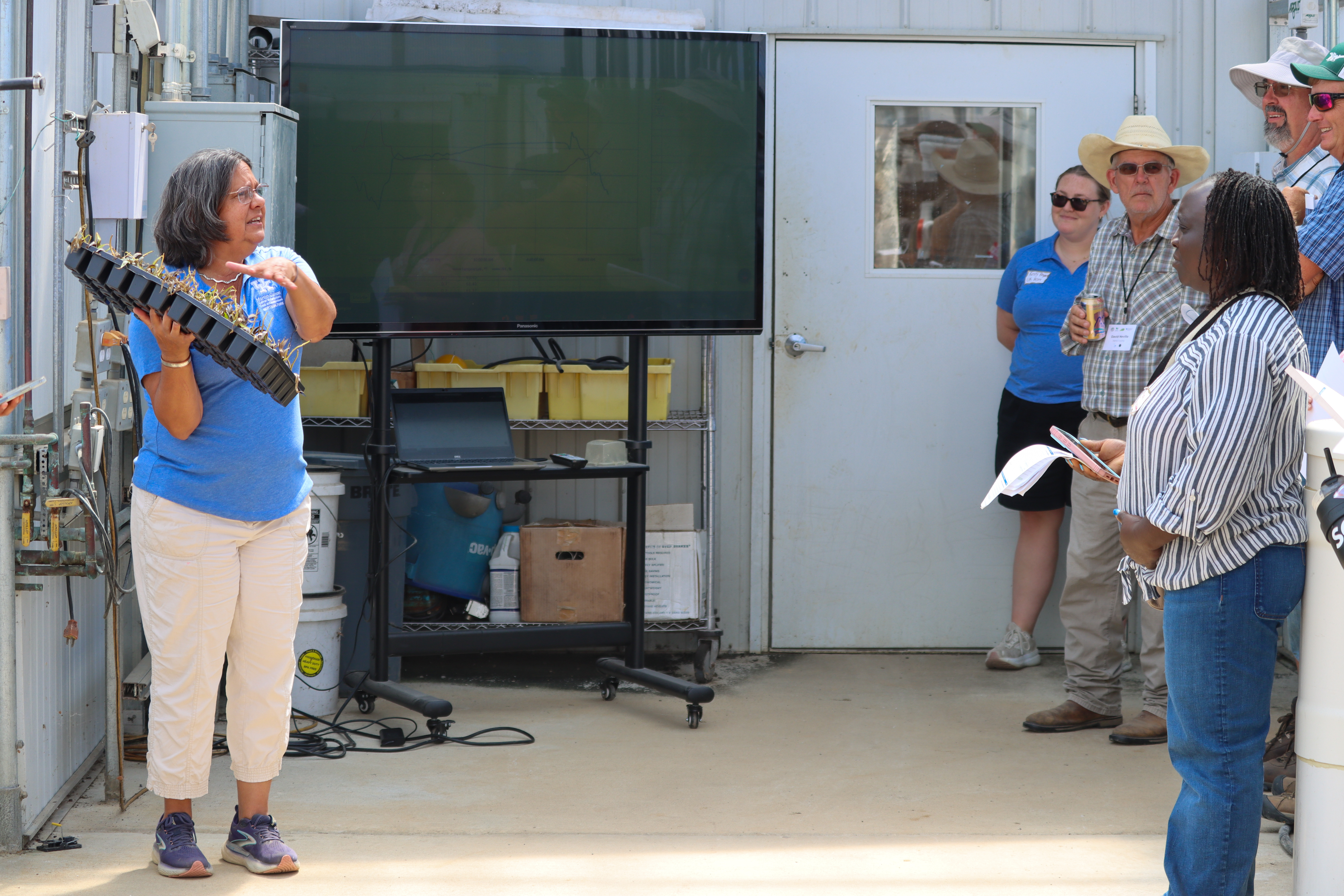 Woman in greenhouse talking to participants 