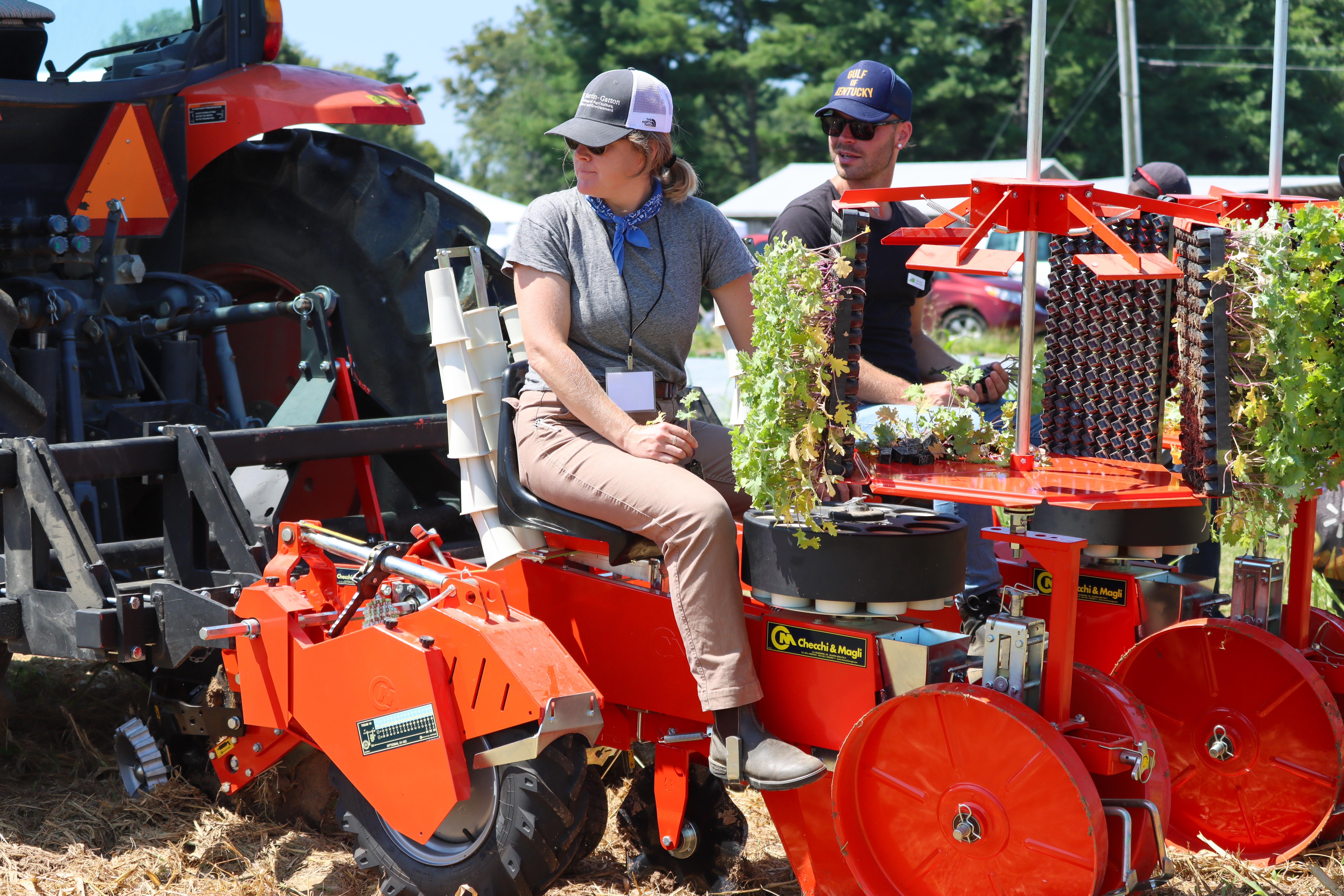 2 people in hats sitting on a red tractor 