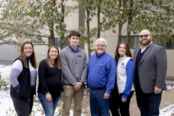 team of people standing together smiling in front of some trees with snow on the ground. 