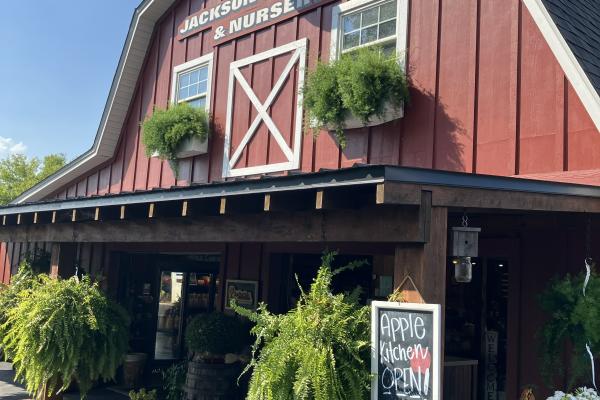 A photo of the exterior of Jackson's Orchard. It is a red barn with a sign displaying "Apple Kitchen OPEN!"