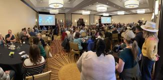 large group of people in conference room facing away from camera toward presenter at front