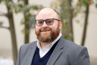 man smiling in front of blurred trees in background
