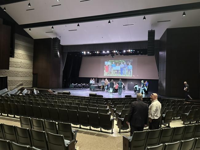 performing arts center with chairs in foreground and tables and projector screen on stage