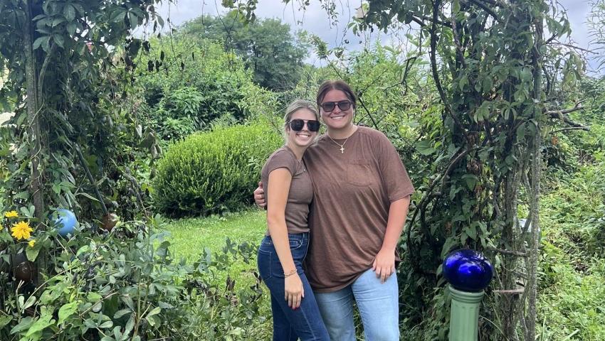 two people standing under a plant covered arch
