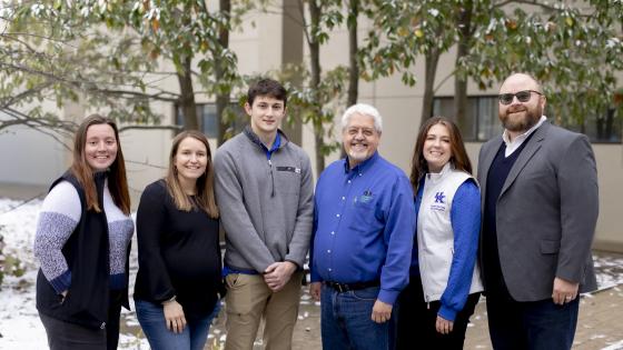 team of people standing together smiling in front of some trees with snow on the ground. 