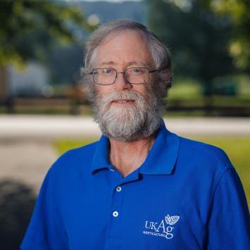 man in blue shirt standing in front of grass and concrete