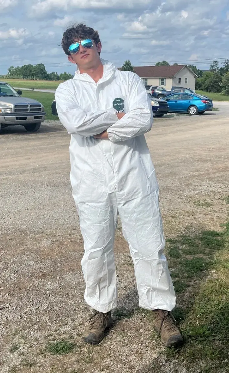 man standing with arms crossed in white fumigation suit with boots and sunglasses